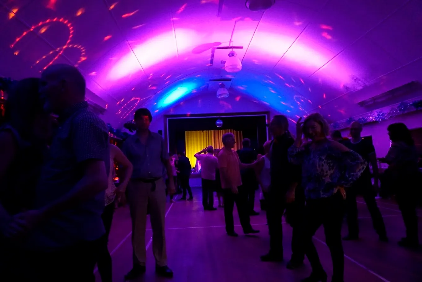 Main Hall set up for a tango social — sprung wooden floor lit with disco lighting, dancers in the foreground