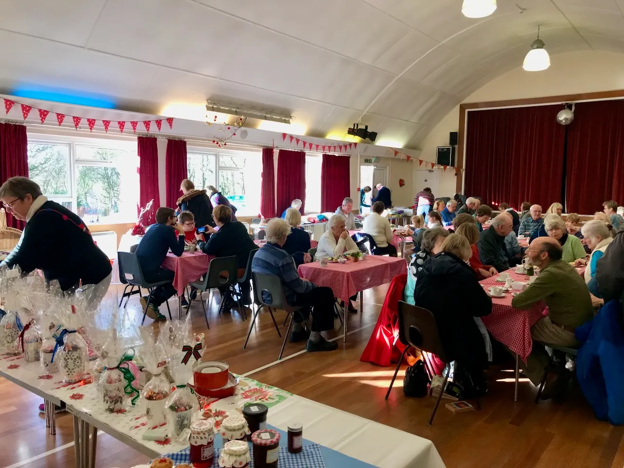 The Main Hall set up for a community coffee morning — red gingham tablecloths, bunting strung across the curved ceiling, tables of guests chatting
